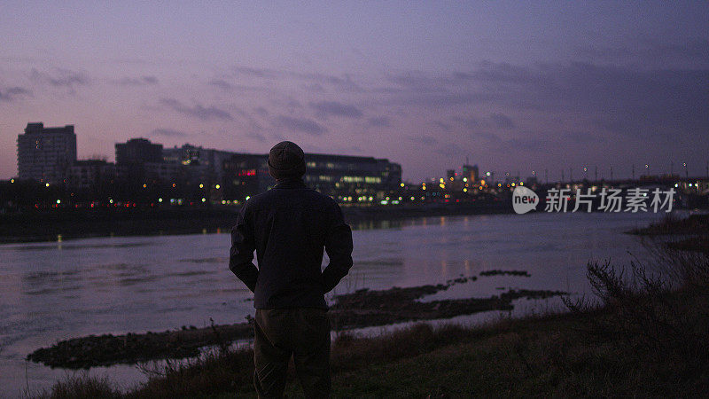 河畔美丽的日落。城市天际线的背景。欣赏风景的男人