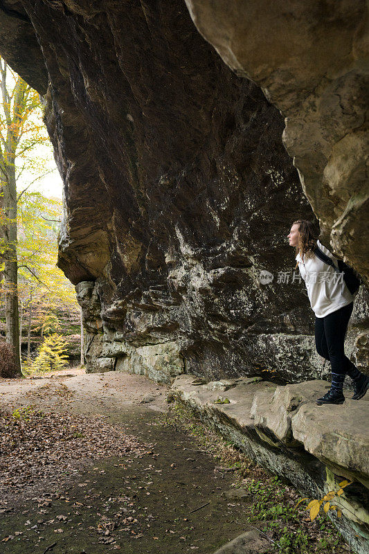 在美国伊利诺斯州众神花园附近的庞德山谷徒步旅行路线上，一个金发的白人少女从一个开放的山洞里抬头仰望