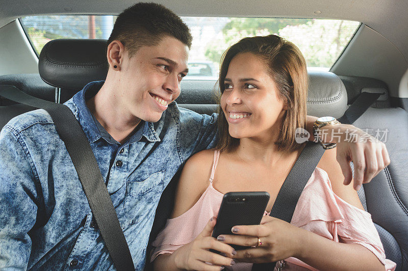 一对年轻夫妇在汽车后座上看智能手机