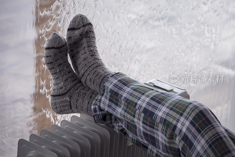 近距离影像的女人的腿在羊毛袜在散热器加热器在降雨的冬季。