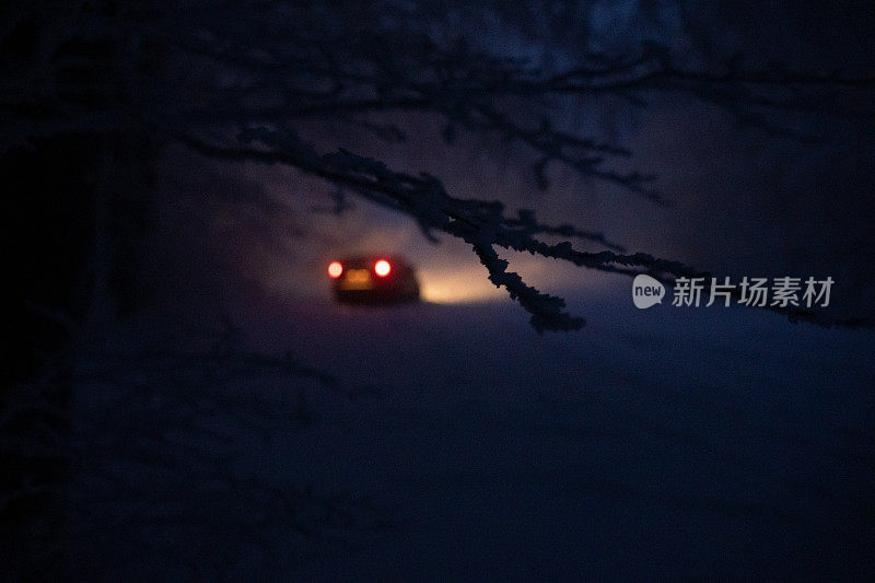 司机POV在积雪覆盖的道路上行驶，初雪飘落。被前灯和前车的红绿灯照亮的路。