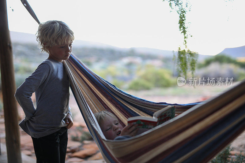 一个小男孩躺在吊床上看一本平装书。
