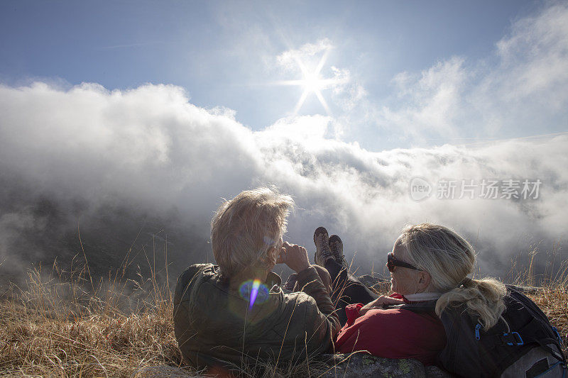 早晨，成熟的情侣徒步旅行者在长满草的山坡上放松