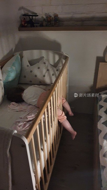 安静的小女孩睡在她舒适的婴儿床里，她的腿在婴儿床围栏之间蹦着