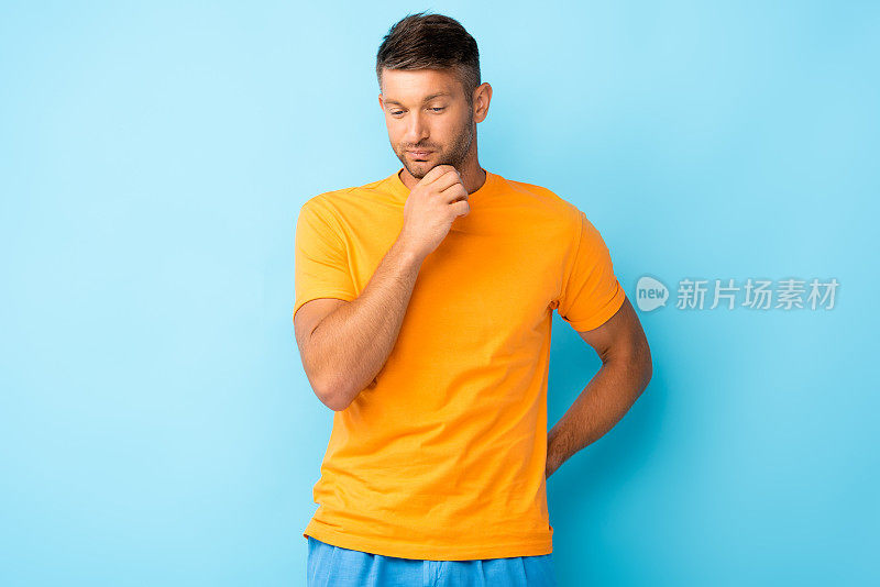 穿着黄色t恤的深思熟虑的男人俯视着蓝色