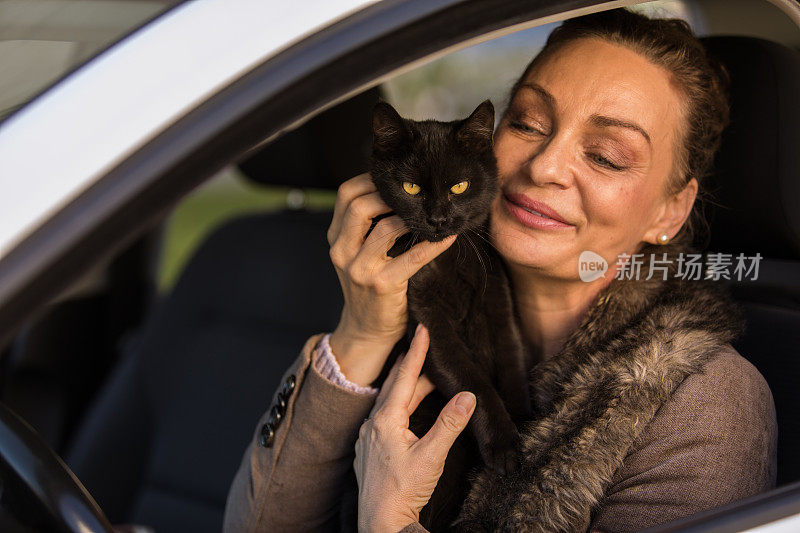 快乐成熟的女人坐在她的车和她的黑猫