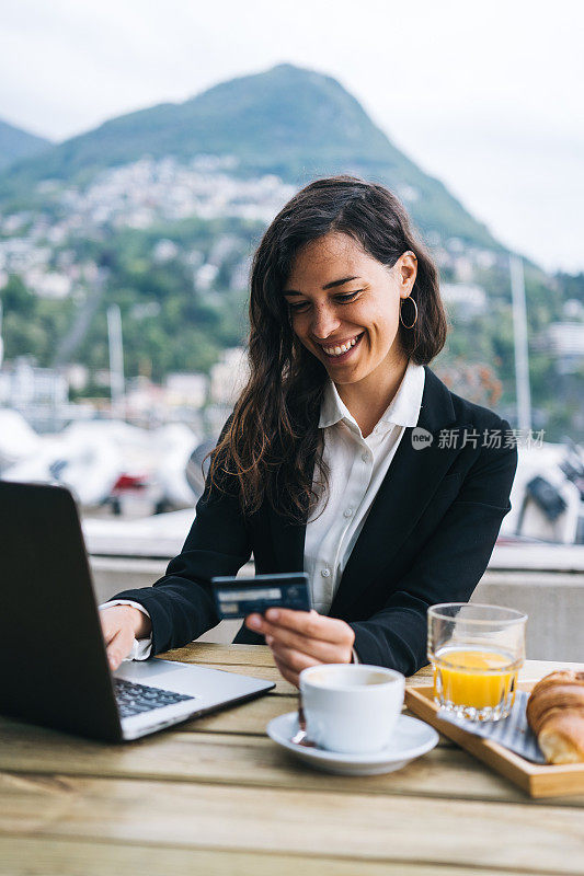 年轻的商业女性在户外咖啡馆使用信用卡