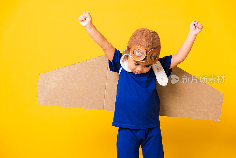小孩小男孩微笑着戴着飞行员帽玩，护目镜和玩具纸板飞机机翼