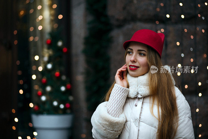 可爱的金发女人，红唇，戴着滑稽的帽子和冬衣走在装饰着花环的街道上。空间的文本