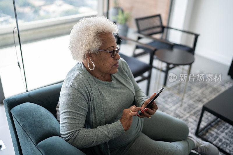 一位资深女性坐在家里的沙发上使用智能手机