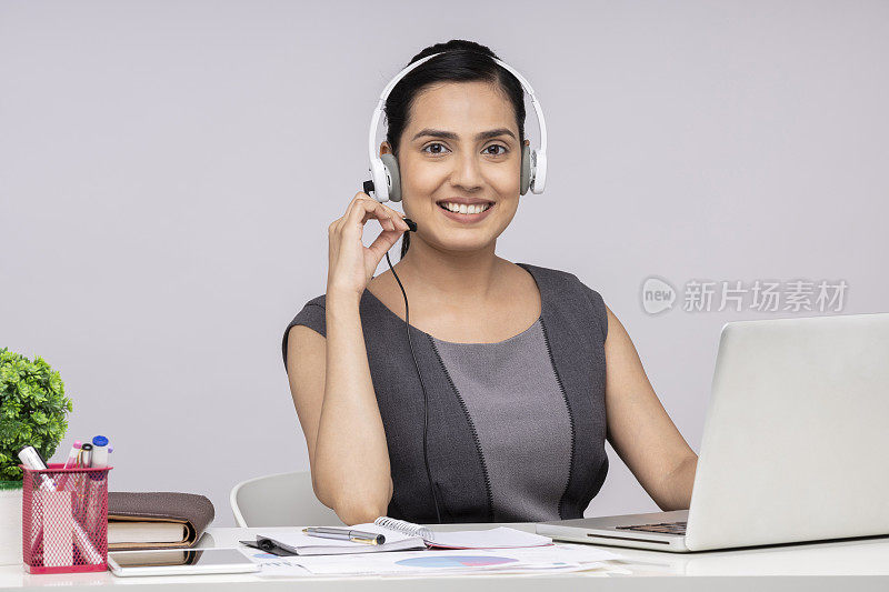一个有吸引力的年轻商业女性的肖像使用耳机和耳机使用笔记本电脑坐在孤立的白色背景