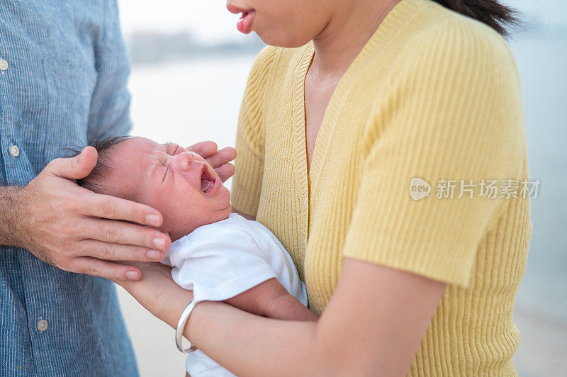 母亲和父亲在海边安慰哭泣的新生儿男婴在海滩日落