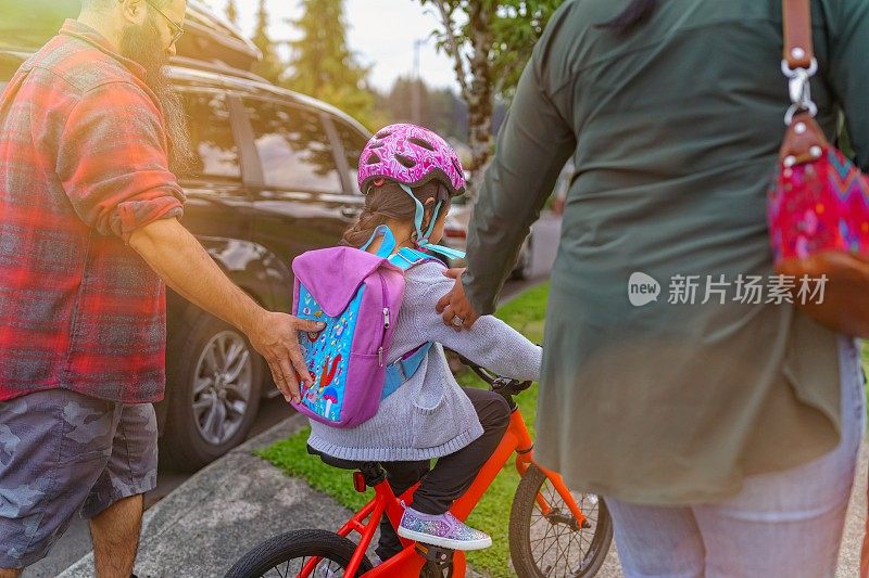 小女孩在父母的帮助下学习骑自行车