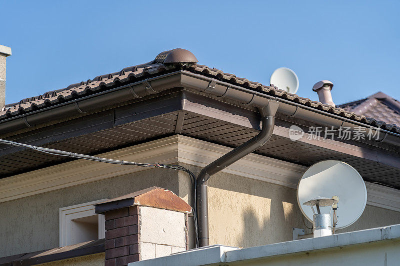 新的现代灰泥屋顶与棕色山墙金属屋顶，卫星盘和天沟管道系统在蓝色天空复制空间背景。房地产的概念。