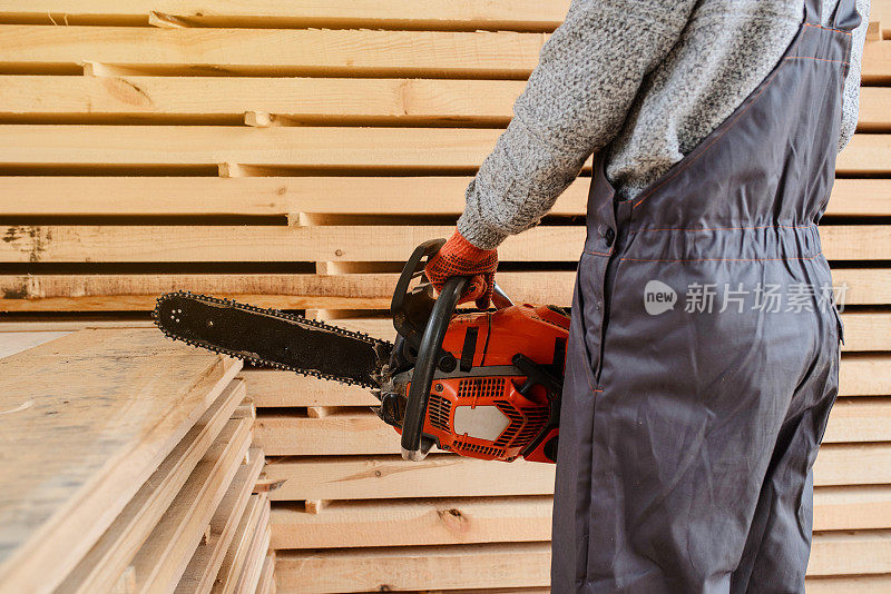 近距离观察木制仓库里的木匠小伙子，他手里拿着一把链锯，锯着木板。