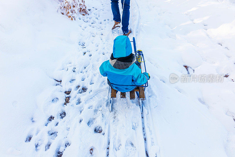 蹒跚学步的男孩在雪橇上，他的父亲拉着他