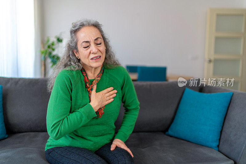 一名老年妇女坐在家里的沙发上感到胸口疼痛