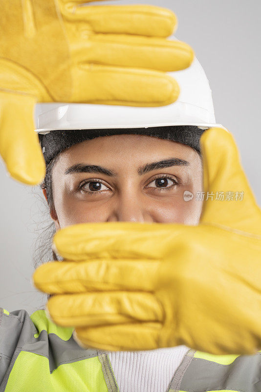 一名戴白色安全帽、黄色安全手套和反光背心的女工程师。
