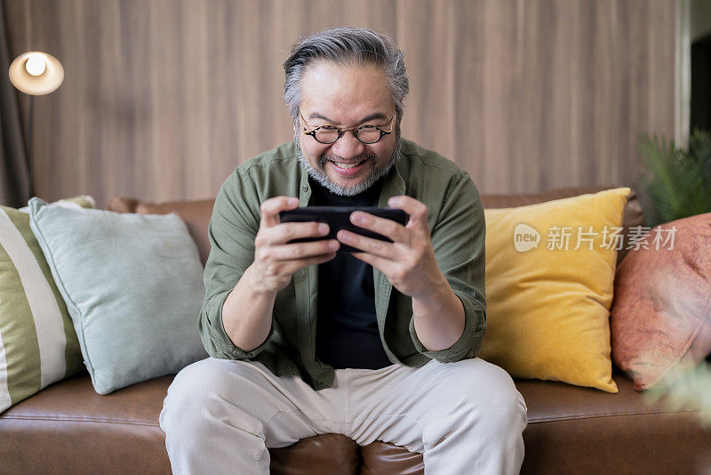 亚洲成年成熟男性网络游戏成瘾，退出有趣的亚洲男人笑微笑手玩电子竞技数字游戏虚拟在线智能手机与世界各地的在线朋友竞争特写镜头在家里