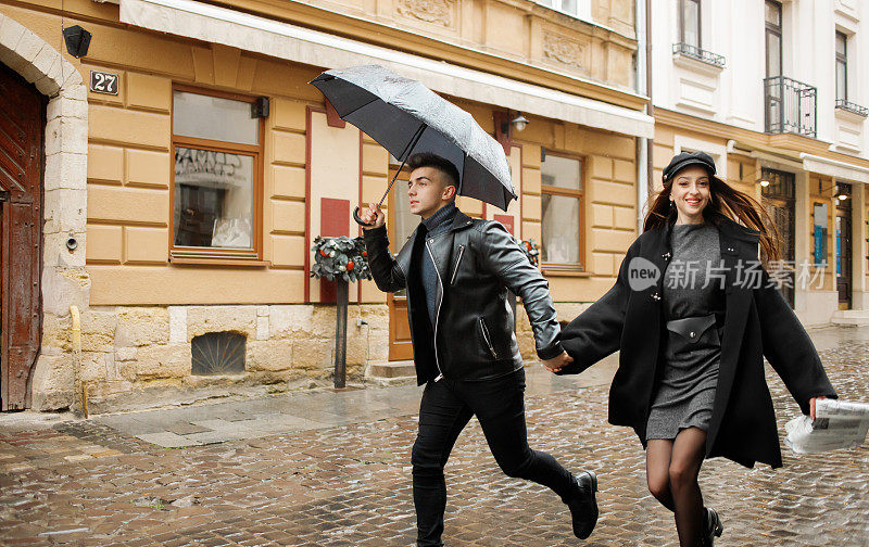 一对豪华夫妇在雨天跑在街上。那个人手里拿着一把伞。2019年11月2日，乌克兰利沃夫。