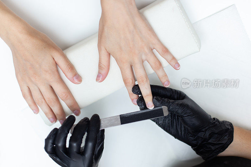 美甲师在美甲沙龙用指甲锉锉女顾客手上的指甲