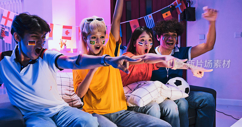 一群快乐的亚洲年轻人在家里看电视上的足球比赛，晚上一起欢呼庆祝进球。2022卡塔尔多哈世界杯，体育迷的支持者，或朋友聚会的概念
