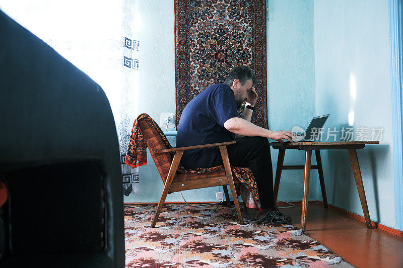 成熟的男人在家庭房间的笔记本电脑前工作