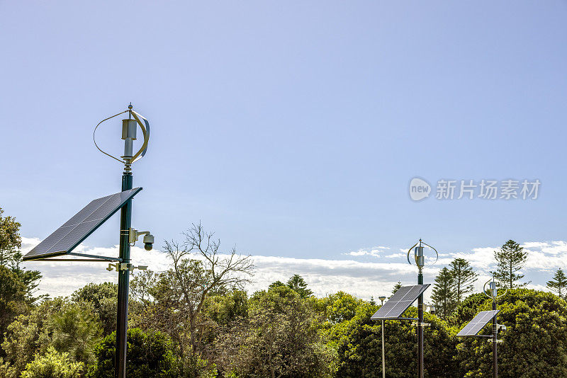 三个小型太阳能电池板与风力发电机，正面视图，蓝天背景与复制空间