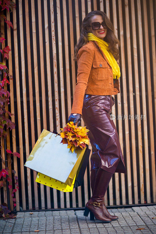 穿着棕色风衣带着购物袋微笑的时尚女人