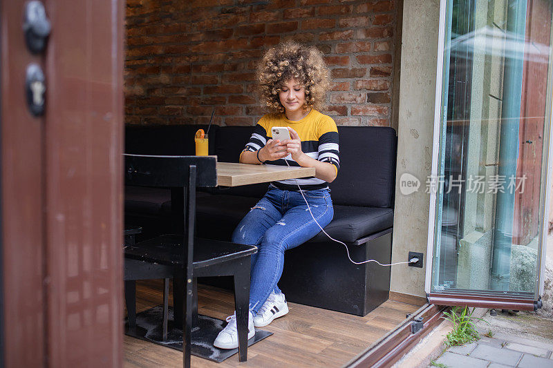 一个留着非洲式发型、面带微笑的年轻女子坐在酒吧里玩手机。