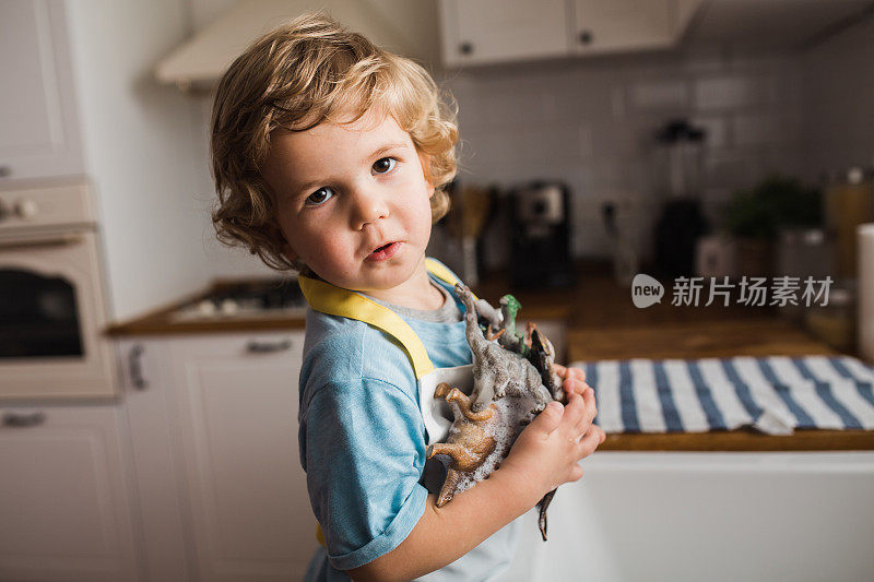 小男孩在厨房的水池里玩，用水洗恐龙玩具
