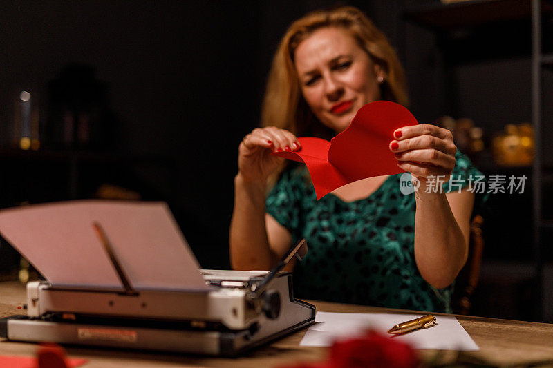 女人手里拿着一颗红纸心，她正在撕中间