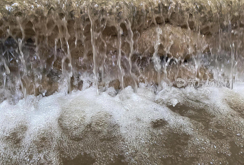 一个瀑布的水流过石墙，喷泉的水流过岩石和水面的照片。