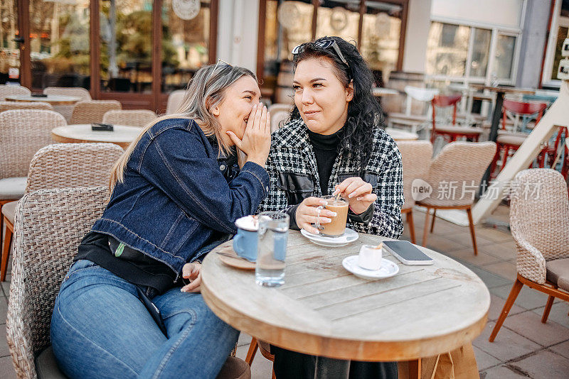 两个年轻女子坐在咖啡馆外面喝咖啡