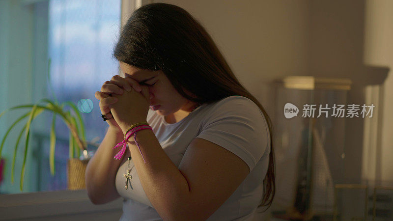 天主教南美年轻女子在家里祈祷，双手紧握，虔诚，背景是圣母玛利亚。虔诚的宗教人士强烈祈祷