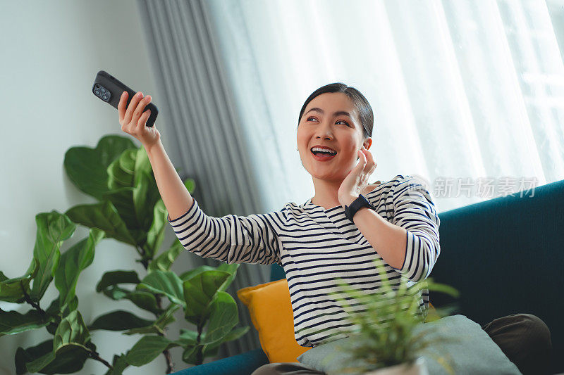 快乐的女人在家里用智能手机和耳机听音乐。