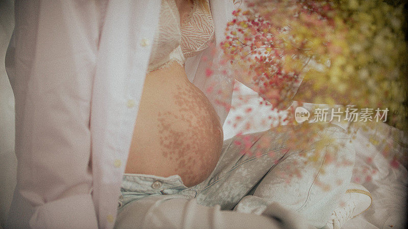 女人的手抚摸着她怀孕的肚子，上面映着花朵的影子。