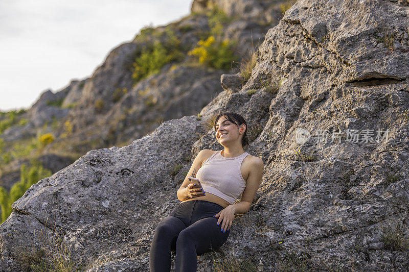在成功的户外训练后，女孩坐在岩石上享受着良好的氛围和新鲜的空气。