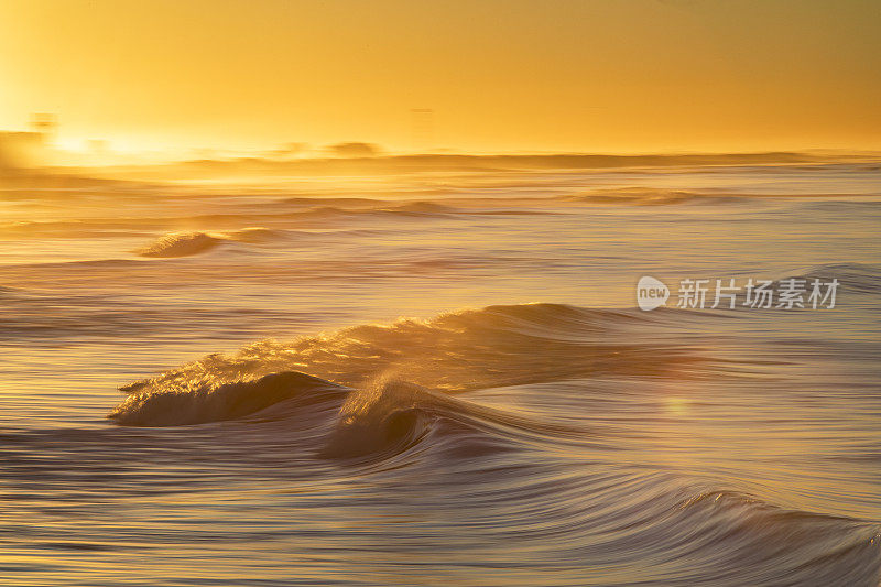 在海滩上戏剧性的日出期间，平滑的金色海浪的海景