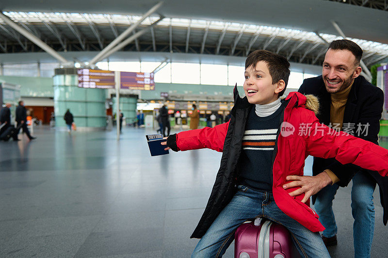 在国际机场候机大厅，兴高采烈的爸爸和他可爱的儿子在行李箱里玩耍，等待办理登机手续