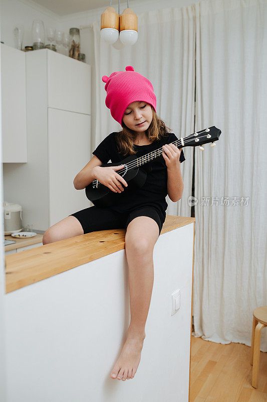戴着粉红色帽子的小女孩坐在高桌上弹着古塔莱琴。