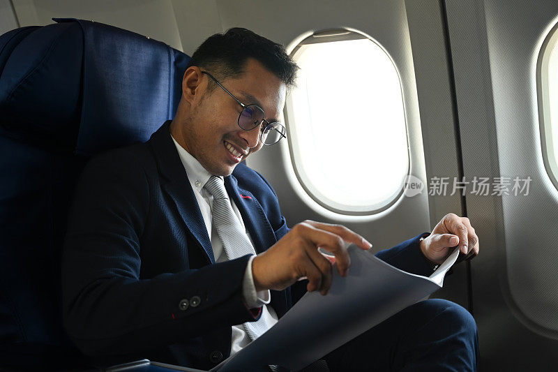 穿着正装的讨人喜欢的商人坐在机舱舒适的座位上阅读商业报纸。