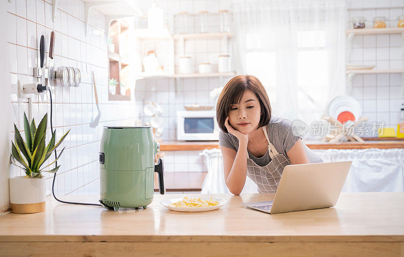 亚洲厨师女孩在厨房用空气炸锅机煎土豆的肖像。居家办公生活新常态。科技环保家居智能设备，亚洲家庭主妇，简约概念