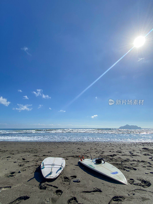 海滩上放着两块冲浪板，远处有许多冲浪者在冲浪