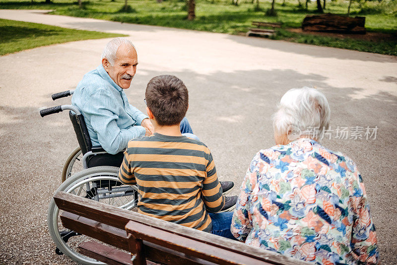 照顾轮椅上的爷爷的孩子。他们一起坐在公园的长椅上玩得很开心。