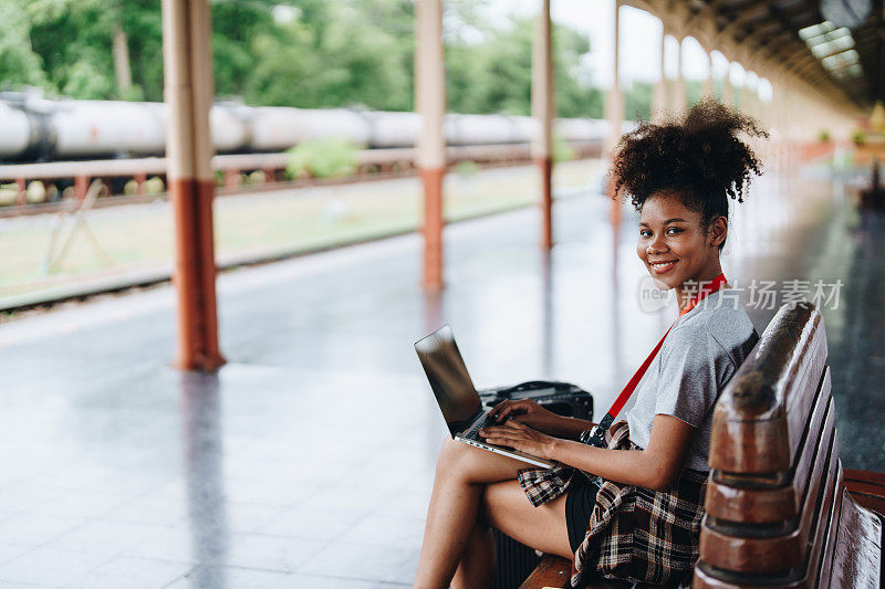 亚洲少女，非洲裔美国人在车站等火车时使用电脑笔记本电脑旅行。