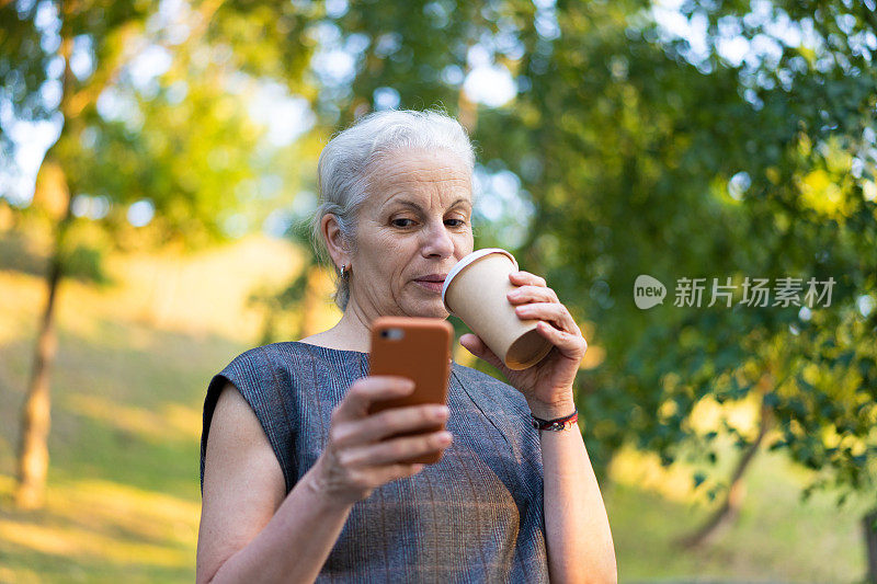 白发苍苍的西班牙裔高级商务女士在户外使用智能手机。夏天在公园散步的老妇人喝着咖啡。