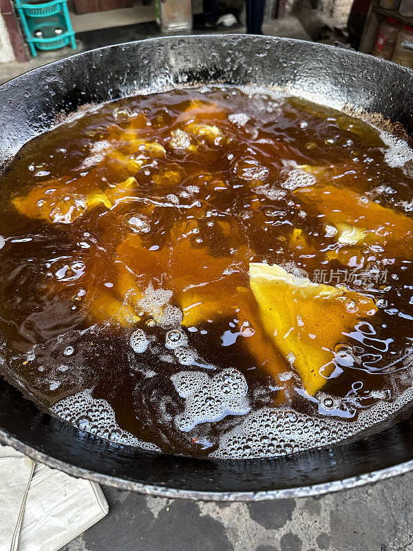 在karahi(印度炒锅)中油炸的一批samosas的特写图像，冒泡的热油，印度街头小吃摊，不健康的饮食，高架视图