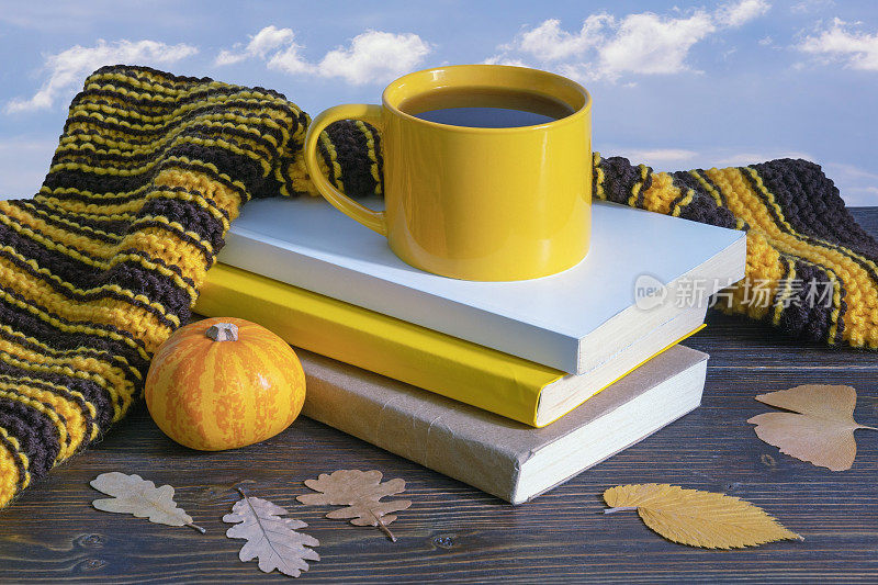 秋天。一叠书，温暖的围巾，黄色的树叶和一杯咖啡放在质朴的桌子上