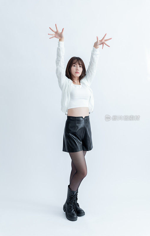 一名身穿白色露膝上衣、黑色皮短裤和长靴的亚洲女性摆出双臂朝天的姿势